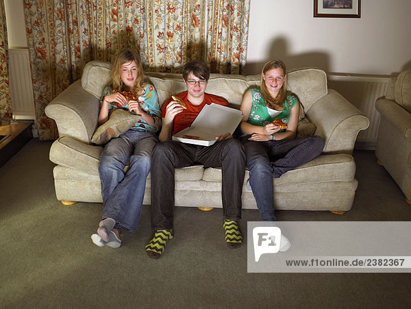 Females and male on sofa  eating pizza