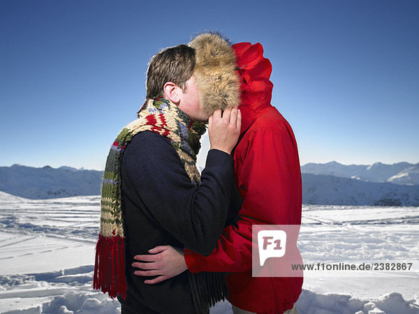 Mann küsst Frau auf Berggipfel