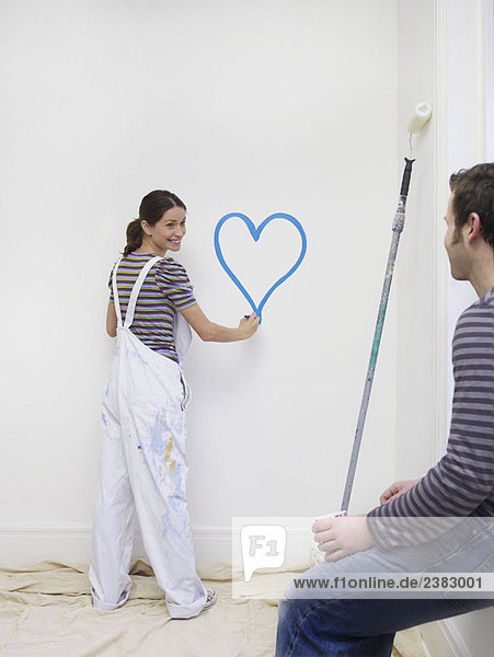 Young woman painting heart on wall