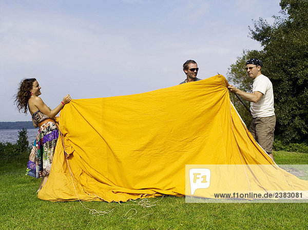 Drei Personen bauen ein Zelt auf