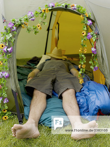 Mann schläft im Zelt mit Hut im Gesicht