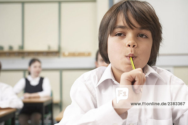 Junge mit Bleistift im Mund  im Klassenzimmer