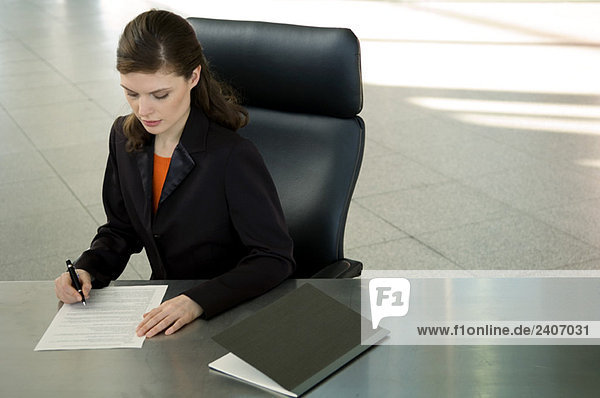 Geschäftsfrau sitzt am Schreibtisch und unterschreibt Dokumente