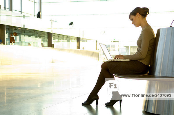 Side profile of a businesswoman using a laptop at an airport lounge