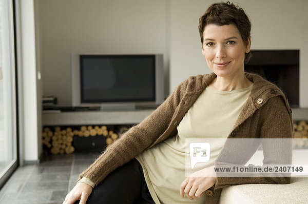 Porträt einer mittleren erwachsenen Frau  die sich gegen eine Couch lehnt.