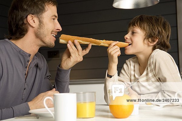 Mid adult man eating a baguette with his son