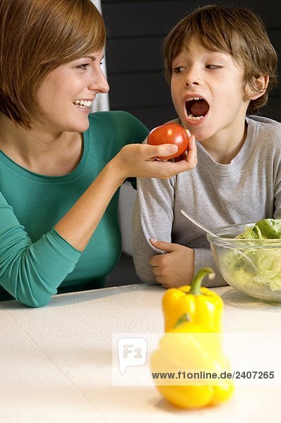 Junge Frau füttert ihren Sohn mit einer Tomate.
