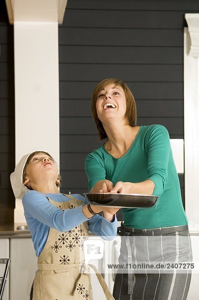Young woman holding a frying pan with her son and smiling