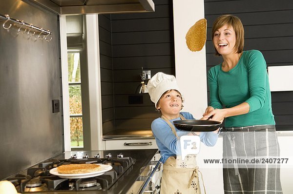 Junge Frau  die mit ihrem Sohn einen Pfannkuchen umdreht.