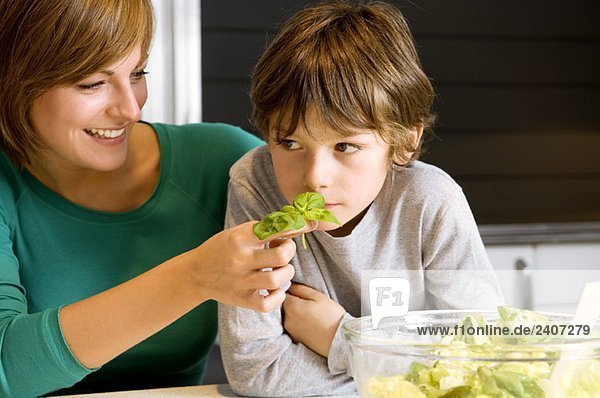 Close-up of a young woman feeding basil to her son