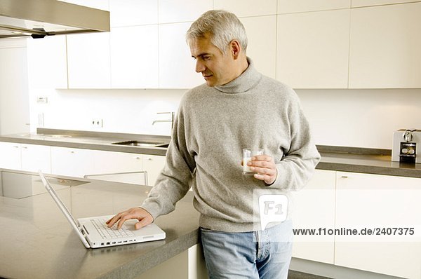 Der reife Mann arbeitet an einem Laptop in der Küche.