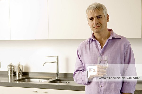 Porträt eines reifen Mannes mit einem Glas Wasser in der Küche