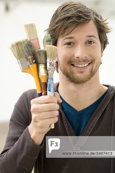 Portrait of a mid adult man holding paintbrushes