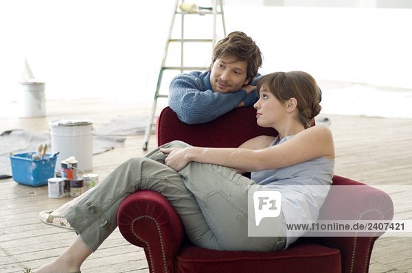 Young woman sitting in an armchair and a mid adult man leaning behind her