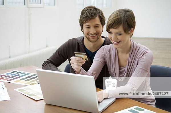 Mittlerer Erwachsener Mann und eine junge Frau  die einen Laptop benutzen und eine Kreditkarte haben.