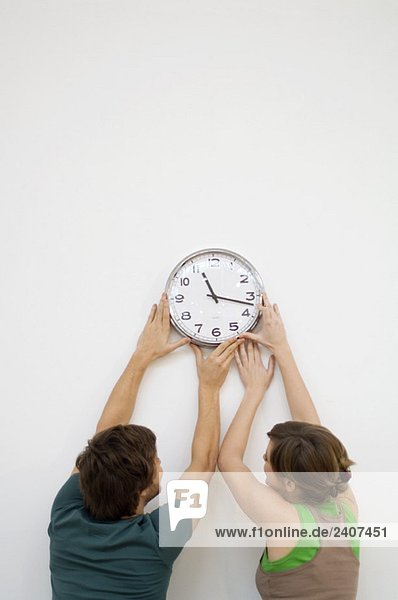 Rückansicht eines erwachsenen Mannes und einer jungen Frau  die eine Uhr an der Wand montieren.