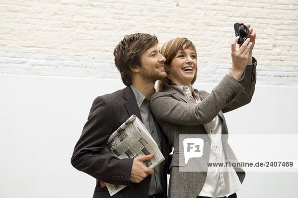 Junge Frau fotografiert mit einer Digitalkamera und einem mittleren Erwachsenen der hinter ihr steht.