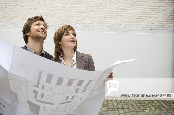 Mid adult man and a young woman holding a blueprint