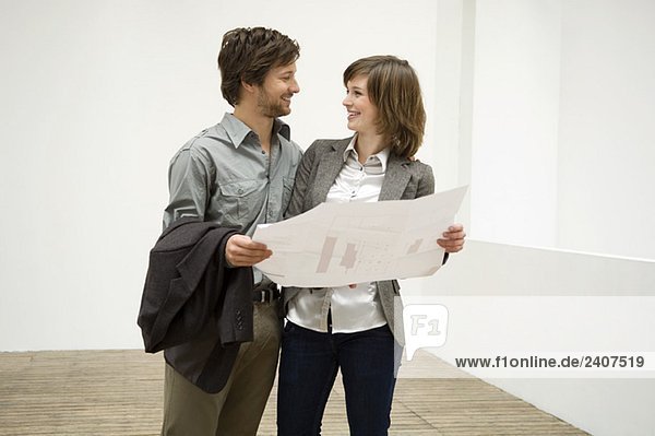 Mid adult man and a young woman holding a blueprint and looking at each other