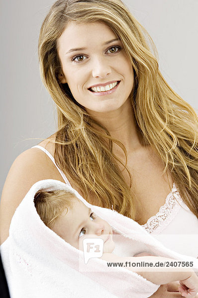 Porträt einer jungen Frau  die ihren Sohn in ein Handtuch wickelt und lächelt.