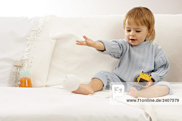 Baby Junge sitzt auf einer Couch und spielt mit Spielzeug