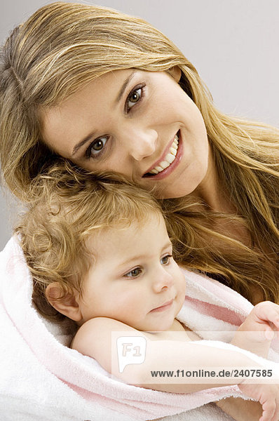 Porträt einer jungen Frau  die ihren Sohn in ein Handtuch wickelt und lächelt.