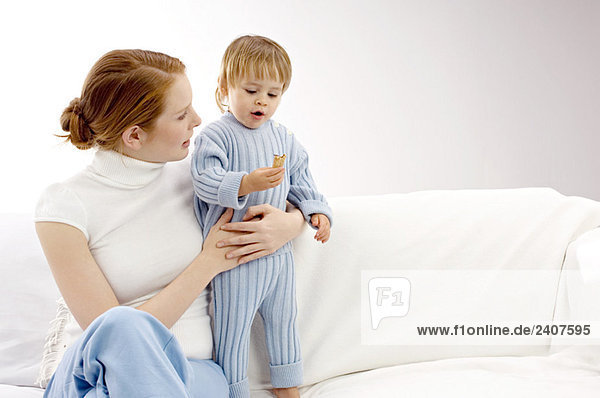 Junge Frau sitzt auf einer Couch  ihr Sohn hält einen Keks.
