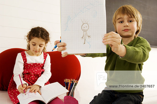 Portrait of a boy showing a drawing with his sister sitting in the background