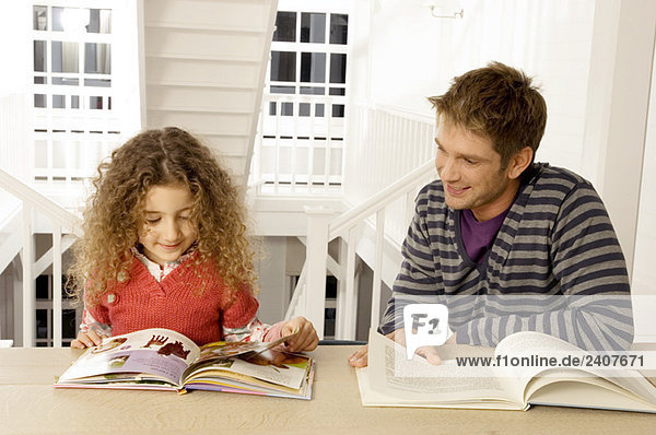 Ein erwachsener Mann sitzt mit seiner Tochter und liest Bücher.
