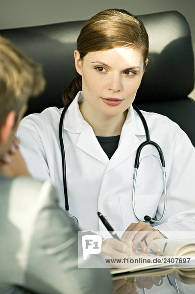 Ärztin sitzt am Schreibtisch und spricht mit einem Patienten