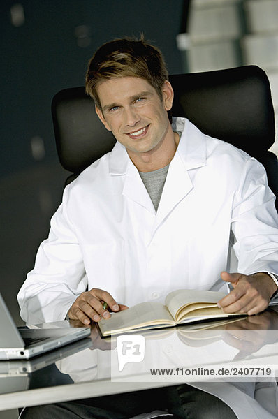 Porträt eines männlichen Arztes am Schreibtisch in seiner Praxis