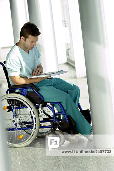 Seitenprofil eines jungen Mannes  der im Rollstuhl sitzt und eine Krankenakte liest.