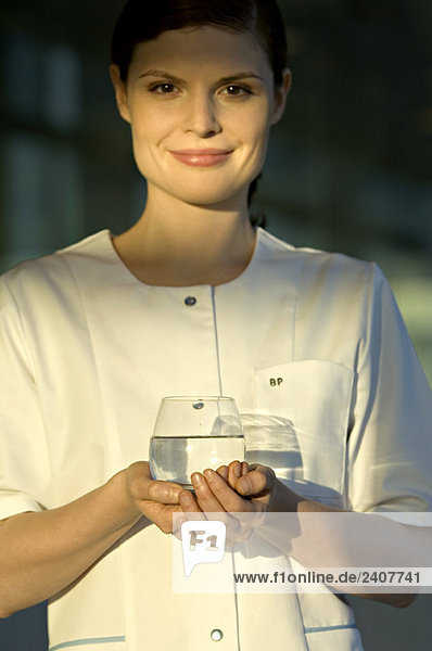 Porträt einer jungen Frau  die ein Glas Wasser hält und lächelt