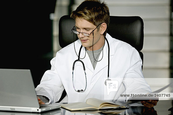 Männlicher Arzt bei der Arbeit an einem Laptop in seiner Praxis