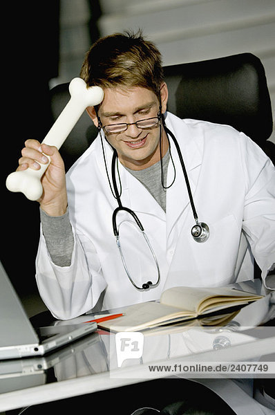 Nahaufnahme eines männlichen Arztes,  der an einem Schreibtisch sitzt und einen Knochen hält.