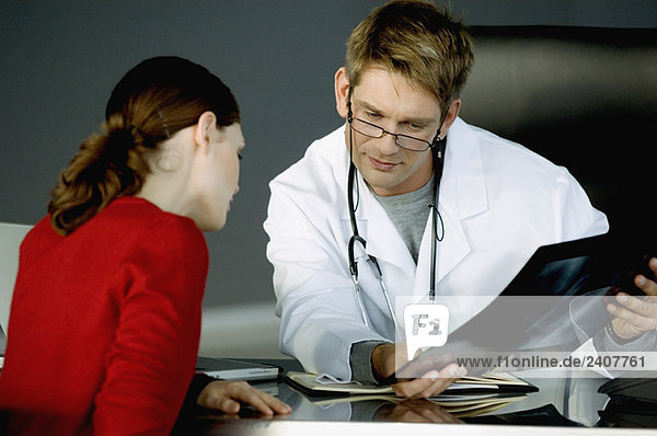 Männlicher Arzt  der einer Patientin einen Röntgenbericht zeigt.