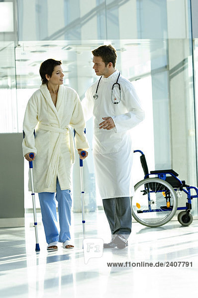 Male doctor assisting a female patient in walking on crutches