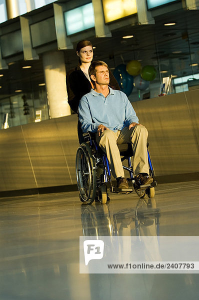 Junge Frau  die einen männlichen Patienten im Rollstuhl schiebt.