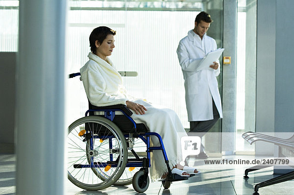 Female patient sitting in a wheelchair and a male doctor standing in the background