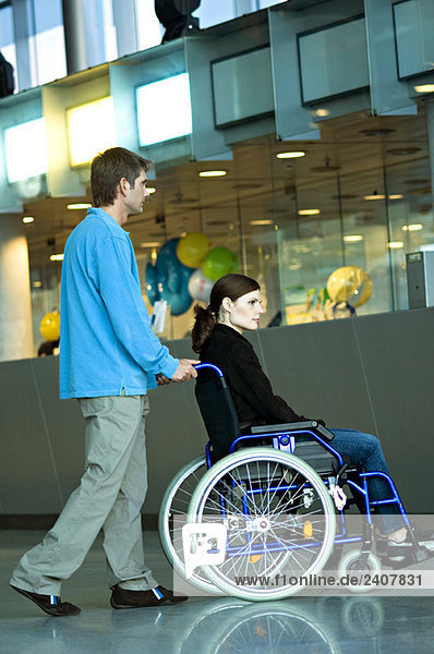 Seitenprofil eines mittelgroßen Mannes  der eine junge Frau im Rollstuhl schiebt.