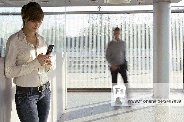 Businesswoman using a mobile phone with a businessman walking in the background