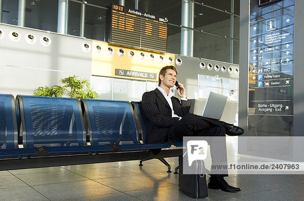 Businessman using a laptop and talking on a mobile phone at an airport lounge