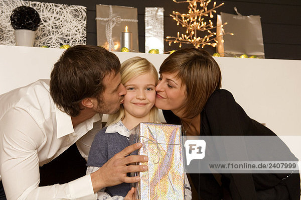 Young woman and a mid adult man kissing their daughter