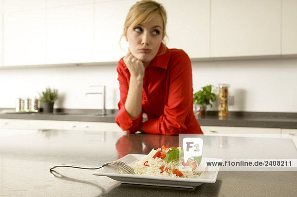 Teller mit Reis vor einer jungen Frau  die sich gegen eine Küchenzeile lehnt.