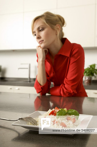 Teller mit Reis vor einer jungen Frau  die sich gegen eine Küchenzeile lehnt.