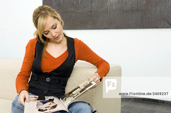 Junge Frau sitzt auf einer Couch und liest eine Zeitschrift.