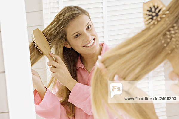 Spiegelung einer jungen Frau  die ihr Haar bürstet
