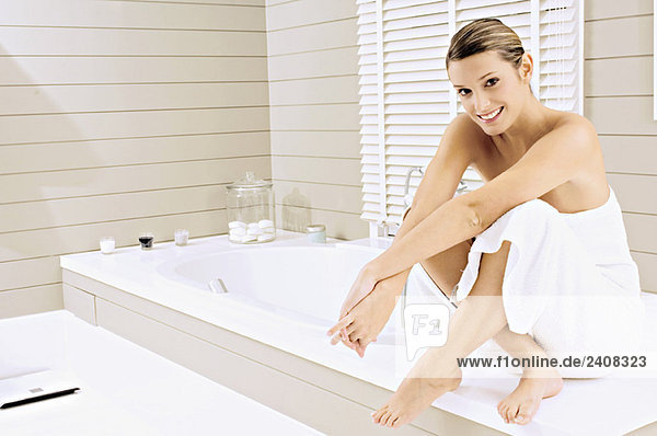 Porträt einer jungen Frau  die auf einer Badewanne sitzt und lächelt.