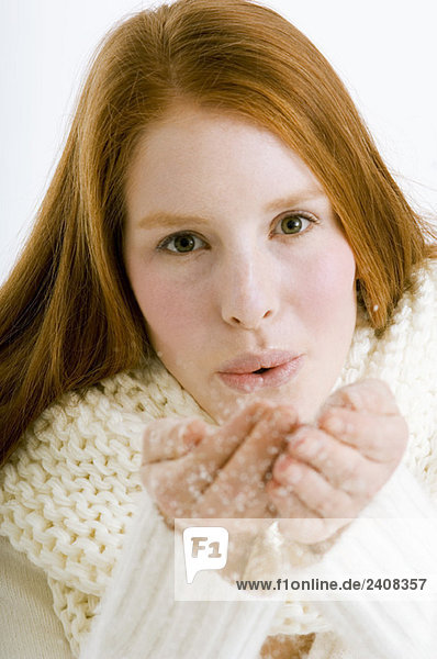 Porträt einer jungen Frau  die Schnee aus ihren hohlen Händen bläst.