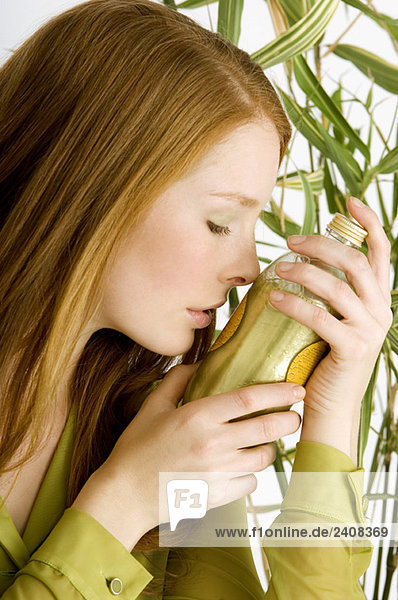 Nahaufnahme einer jungen Frau  die eine Flasche Aromatherapieöl riecht.